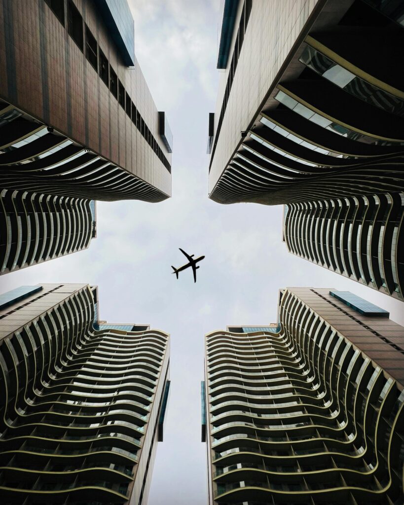 A striking view of a cityscape with modern skyscrapers and an airplane flying overhead.